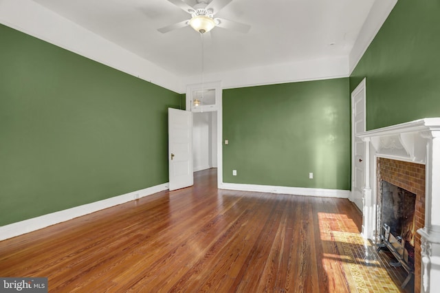 unfurnished living room featuring a ceiling fan, baseboards, dark wood finished floors, and a tiled fireplace