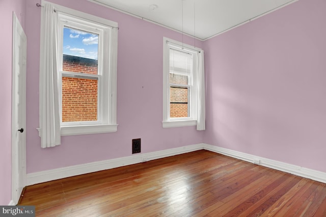 empty room with hardwood / wood-style flooring, visible vents, and baseboards