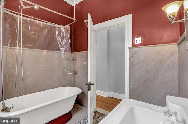 bathroom with a wainscoted wall, curtained shower, a freestanding tub, and tile walls