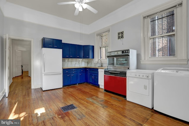 kitchen featuring white appliances, washing machine and dryer, blue cabinetry, and light countertops