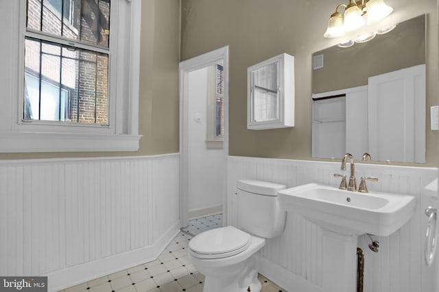 half bathroom with a chandelier, toilet, a wainscoted wall, visible vents, and tile patterned floors