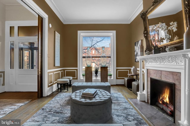 sitting room with wainscoting, a fireplace, crown molding, and wood finished floors