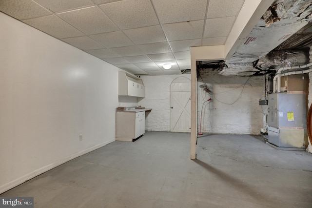 unfinished basement with a paneled ceiling, heating unit, and baseboards