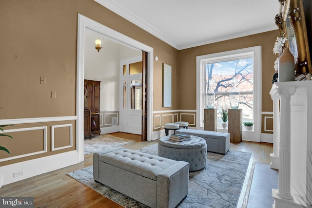 sitting room featuring a decorative wall, a wainscoted wall, light wood-type flooring, ornate columns, and crown molding