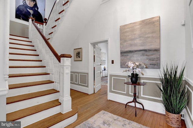 foyer entrance featuring wainscoting, a decorative wall, stairway, and light wood finished floors