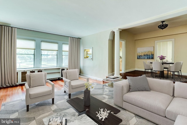 living area with baseboards, wood finished floors, and ornate columns