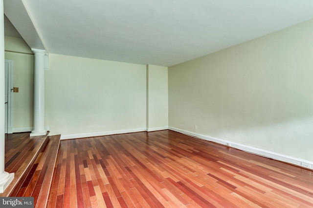 spare room featuring wood finished floors, decorative columns, and baseboards