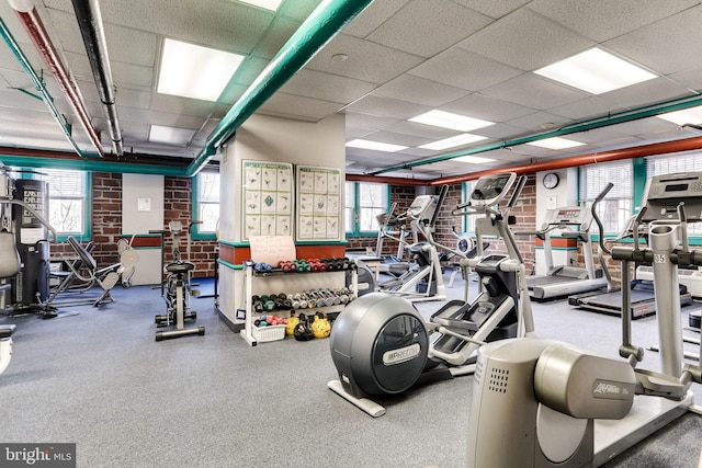 exercise room with a healthy amount of sunlight, brick wall, and a drop ceiling