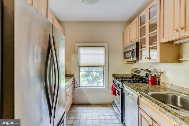 kitchen featuring glass insert cabinets, stainless steel appliances, a sink, and light brown cabinetry