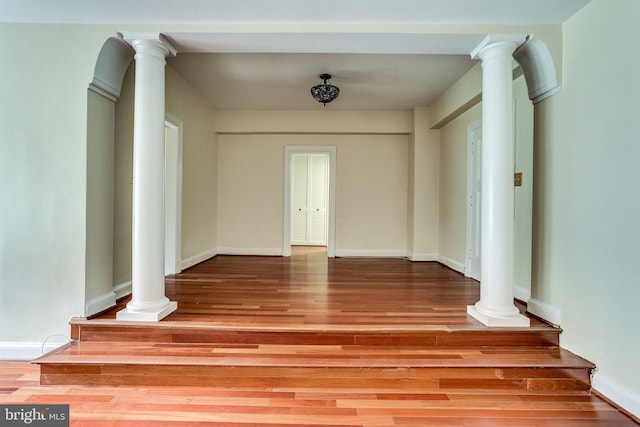 interior space featuring decorative columns, baseboards, and wood finished floors