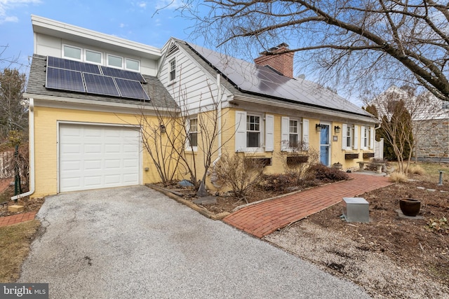 view of front facade with an attached garage, a shingled roof, a chimney, and solar panels