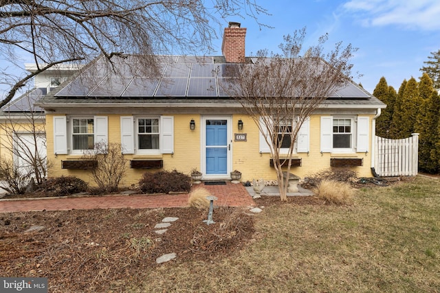 view of front of property with roof mounted solar panels, brick siding, fence, and a chimney