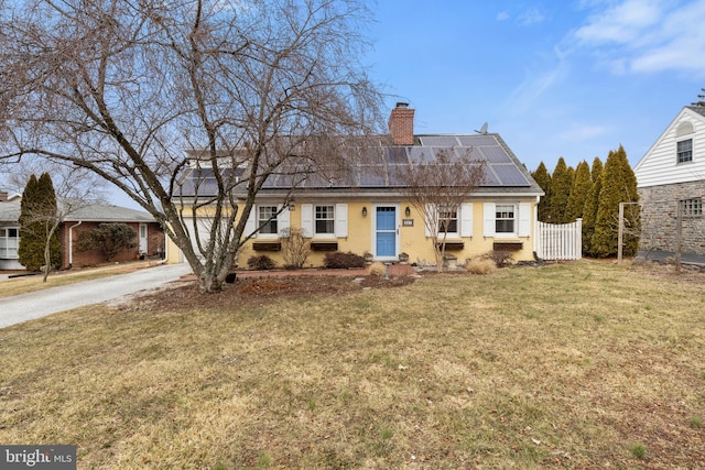 view of front facade featuring a chimney, a front yard, fence, and roof mounted solar panels