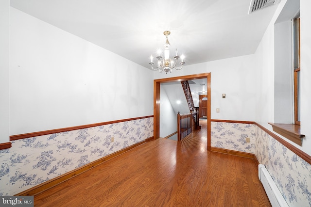 unfurnished dining area with a notable chandelier, visible vents, baseboard heating, wood finished floors, and wallpapered walls