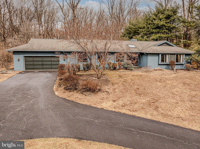 ranch-style home featuring an attached garage, a chimney, and aphalt driveway