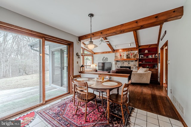 dining space featuring light tile patterned floors, visible vents, a ceiling fan, vaulted ceiling with beams, and a stone fireplace