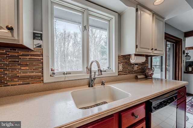 kitchen with light countertops, stainless steel dishwasher, a sink, and tasteful backsplash