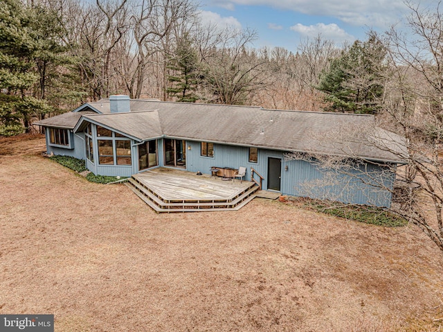 rear view of property featuring a chimney, a sunroom, roof with shingles, and a deck