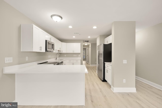 kitchen with white cabinetry, stainless steel appliances, light wood-style floors, a peninsula, and light countertops