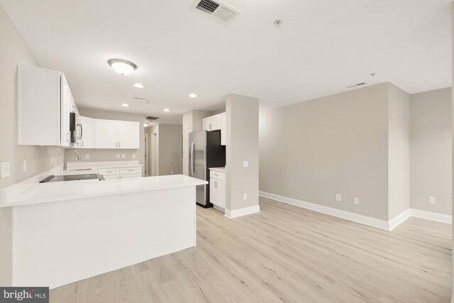 kitchen featuring visible vents, freestanding refrigerator, a sink, light countertops, and light wood-style floors