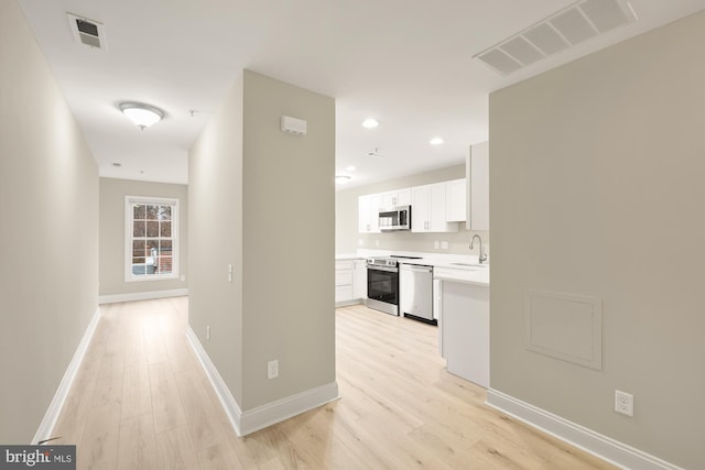 corridor with a sink, visible vents, baseboards, and light wood-style floors