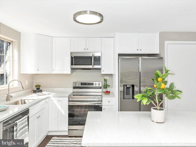 kitchen with light stone countertops, white cabinetry, appliances with stainless steel finishes, and a sink