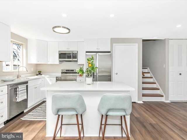 kitchen with white cabinets, dark wood-style floors, a kitchen bar, and stainless steel appliances