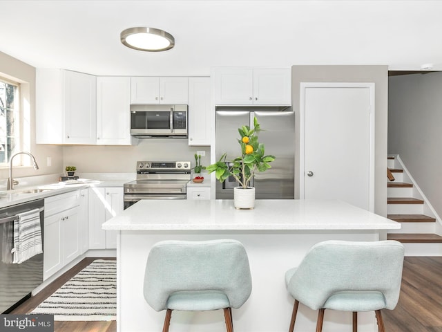 kitchen with a sink, white cabinets, light countertops, appliances with stainless steel finishes, and dark wood finished floors