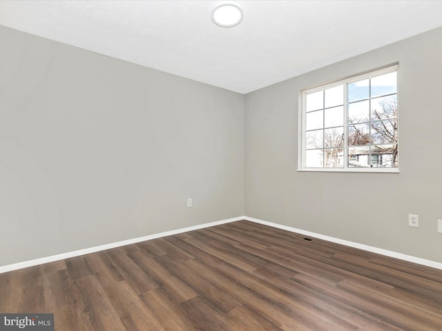 empty room with dark wood-style flooring and baseboards