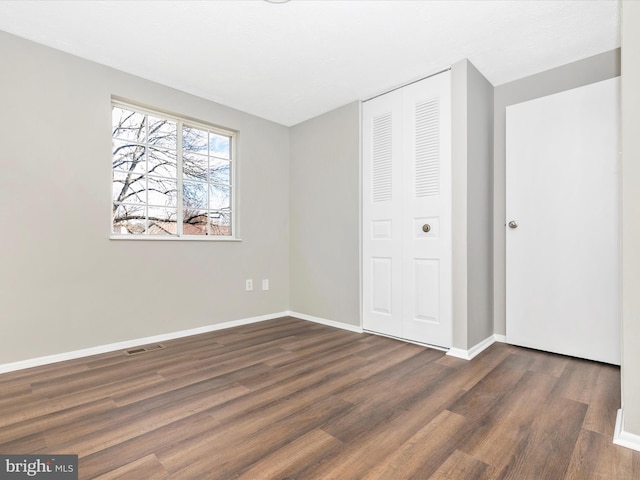 unfurnished bedroom featuring dark wood-style flooring, a closet, visible vents, and baseboards