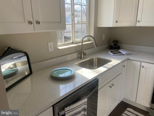 kitchen featuring white cabinets, a sink, dishwashing machine, and light stone countertops