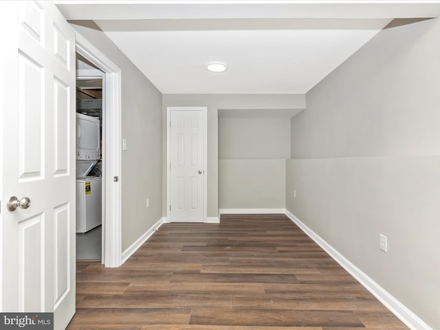 hall featuring stacked washer / dryer, dark wood finished floors, and baseboards