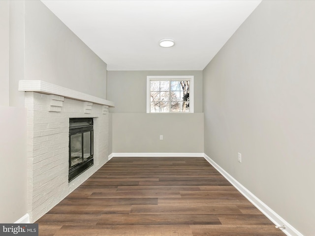 unfurnished living room with a brick fireplace, baseboards, and wood finished floors