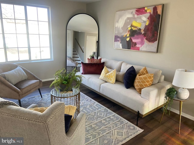 living area with arched walkways, stairway, baseboards, and wood finished floors