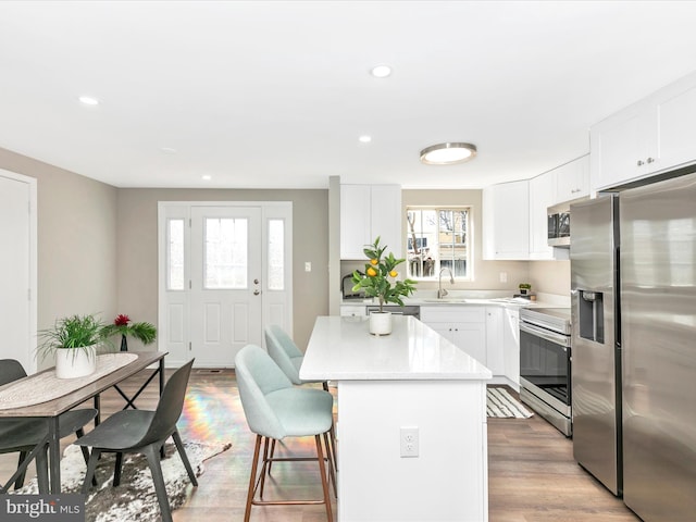 kitchen featuring a center island, a breakfast bar, stainless steel appliances, a sink, and light wood-type flooring