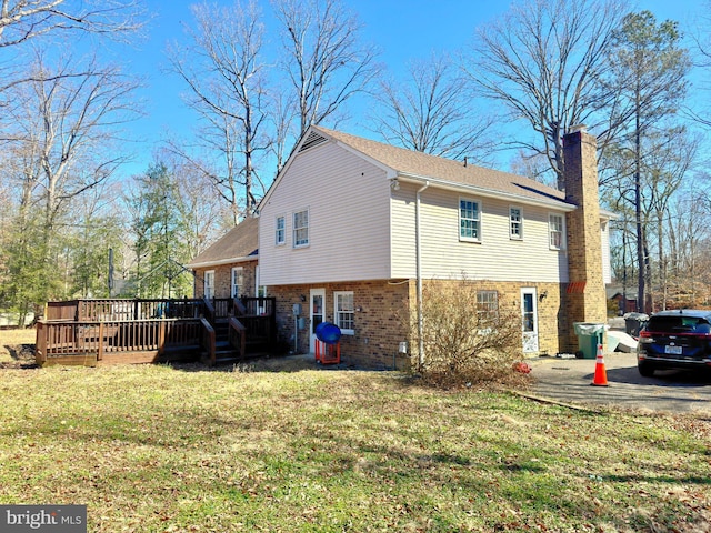 view of side of property with a yard, a chimney, brick siding, and a wooden deck