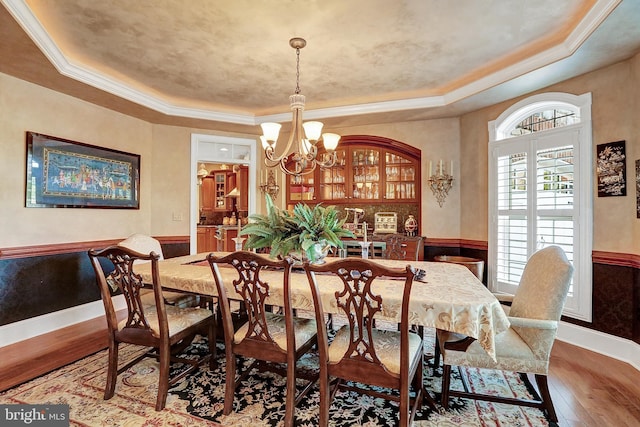 dining space featuring a raised ceiling, wainscoting, crown molding, and hardwood / wood-style floors