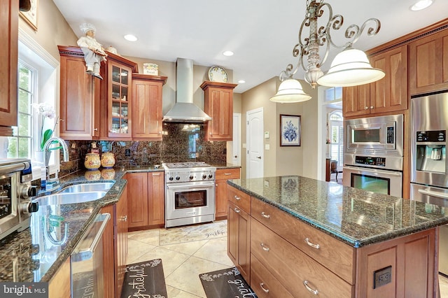 kitchen featuring brown cabinets, stainless steel appliances, tasteful backsplash, a sink, and wall chimney range hood