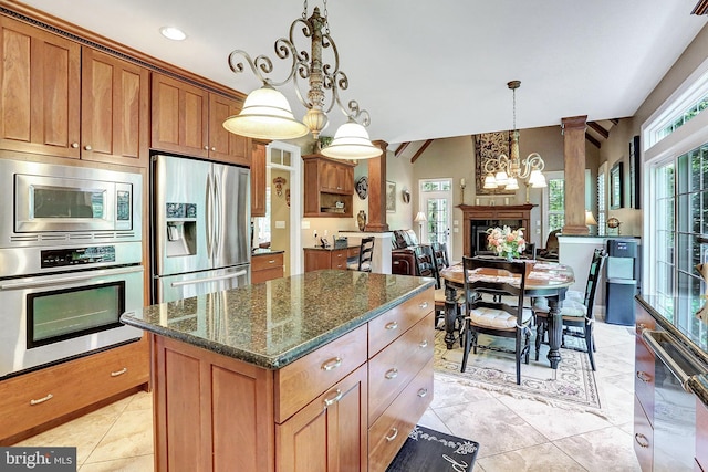 kitchen with appliances with stainless steel finishes, dark stone counters, brown cabinetry, and a fireplace