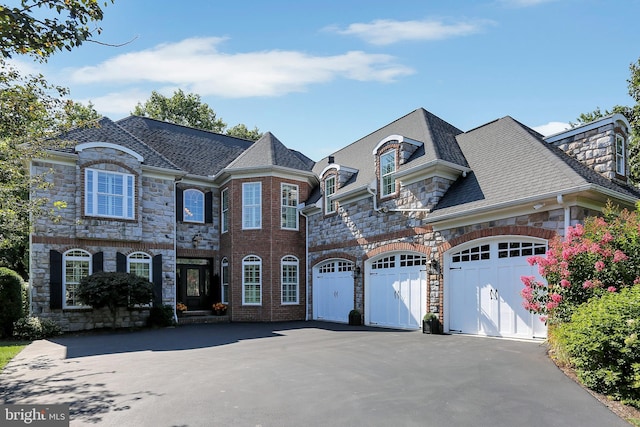 french country inspired facade featuring a garage, driveway, and stone siding