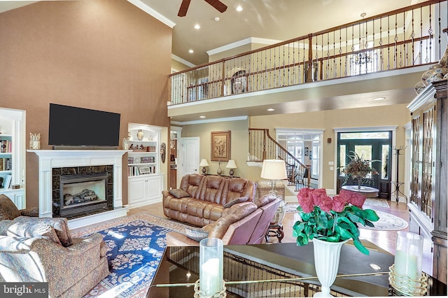 living area with a towering ceiling, ornamental molding, stairs, built in shelves, and a high end fireplace