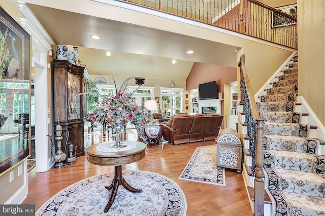 foyer featuring high vaulted ceiling, light wood-style flooring, recessed lighting, a fireplace, and stairway