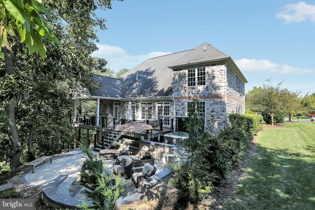 rear view of house featuring stone siding, stairway, a deck, a yard, and a patio area