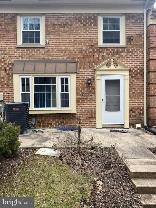 doorway to property featuring central AC and brick siding