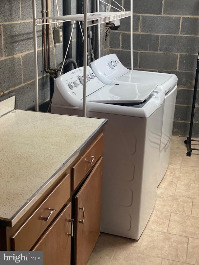 laundry room featuring concrete block wall, cabinet space, and washing machine and dryer