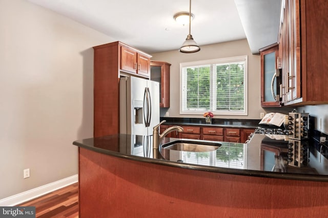 kitchen featuring stainless steel appliances, a sink, baseboards, hanging light fixtures, and dark countertops