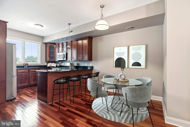 kitchen featuring dark wood-style flooring, dark countertops, visible vents, appliances with stainless steel finishes, and a peninsula