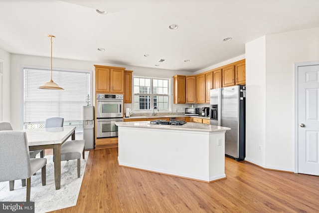 kitchen with a sink, light countertops, appliances with stainless steel finishes, a center island, and light wood finished floors