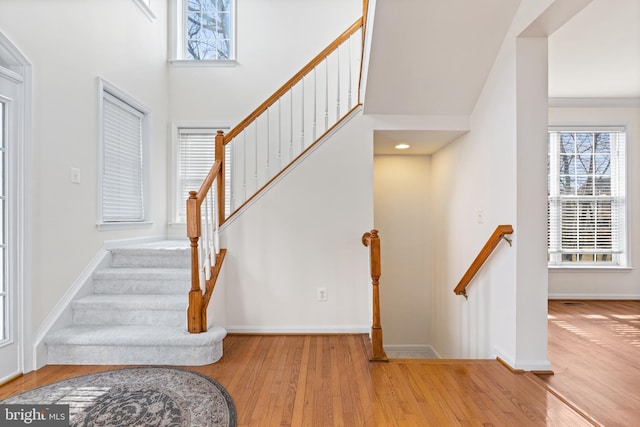 staircase with wood finished floors, a towering ceiling, and baseboards