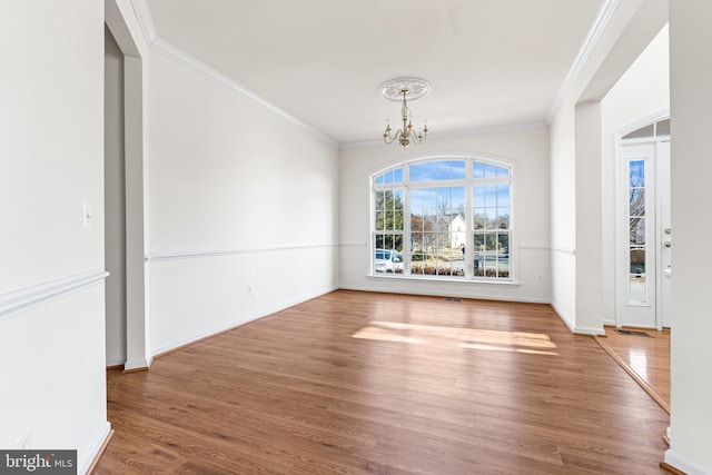 unfurnished dining area with baseboards, visible vents, ornamental molding, wood finished floors, and a notable chandelier